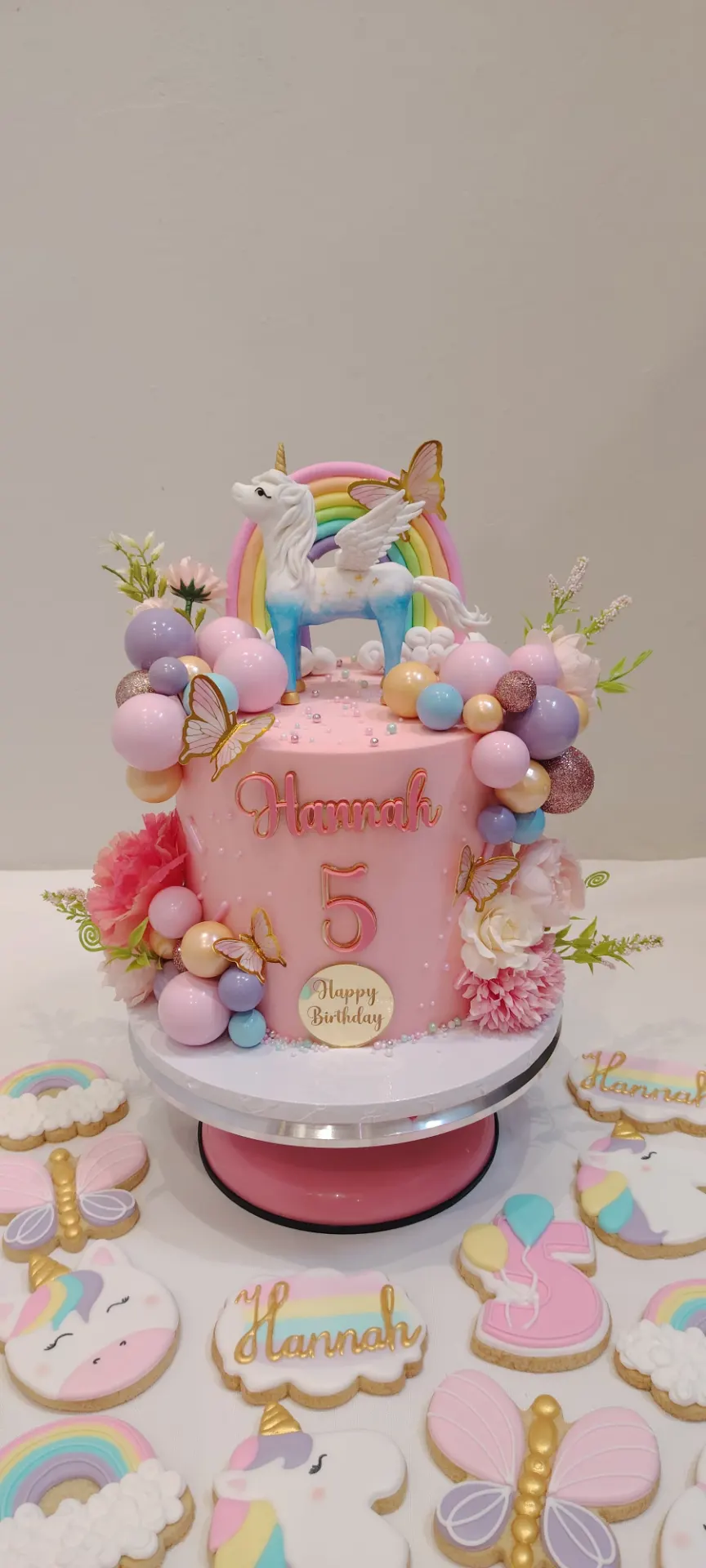 Pink unicorn fifth birthday cake with pastel balloons, rainbow and matching cookies